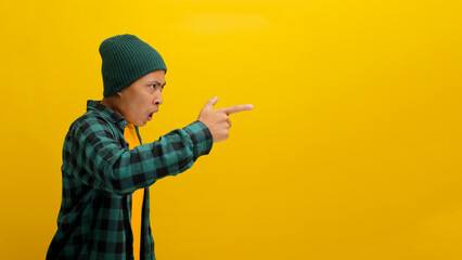 Side view of an Angry young Asian man in a beanie hat and casual shirt is yelling, pointing a...