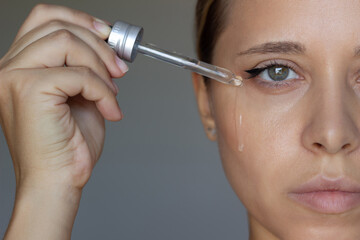 A young caucasian woman applying anti-wrinkle serum to the skin near eyes with a dropper on a dark...