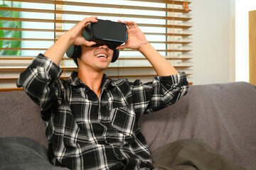 Smiling man wearing VR headset sitting on couch, spending weekend at home