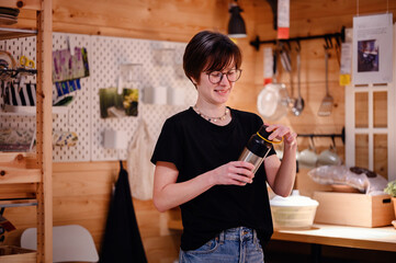 In a homely and rustic kitchen setting, a young adult with glasses is pictured using a thermal...