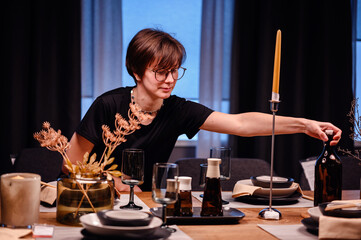 This image features a young adult at an elegantly set dinner table, reaching out to adjust a placement. The sophisticated table setting includes modern tableware and decorative candles, 