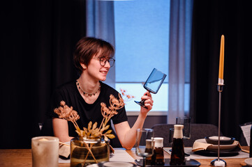 Cheerful moment as a young adult examines a piece of blue glassware at a dining table. The setting...