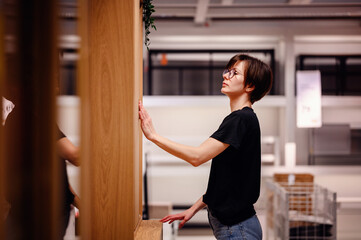 Young adult inspecting a cabinet in a modern furniture store. With a smile and a casual stance,...