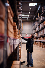 Young woman reaching towards a high shelf in a warehouse, illustrating her focus and determination....