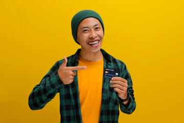 A young Asian man, dressed in a beanie hat and casual clothes, points his finger at a credit card,...