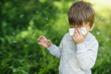 A little boy 4 years old blows his nose into a paper napkin against a background of greenery....