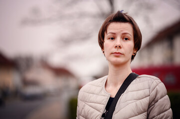 A young woman with short brown hair gazes contemplatively while standing in a suburban...