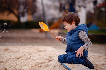 Intently focused, a young boy uses a shovel to play in the sand at a playground, illustrating a...