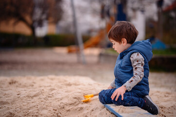 Intently focused, a young boy uses a shovel to play in the sand at a playground, illustrating a...