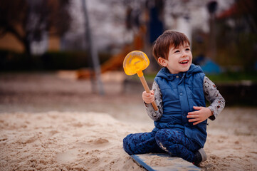 Intently focused, a young boy uses a shovel to play in the sand at a playground, illustrating a...