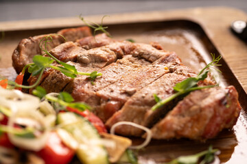 Close-up of beef and pork steak with fresh vegetables on a wooden board.