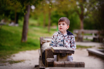 This image beautifully captures a pensive young boy sitting in a wooden structure at a park,...