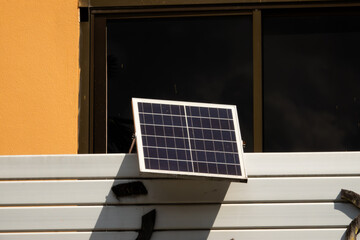 A solar panel is mounted on a wall. The panel is black and white and is on a white wall