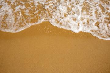 Close-up of soft foamy waves on a sandy beach, depicting serene oceanic textures