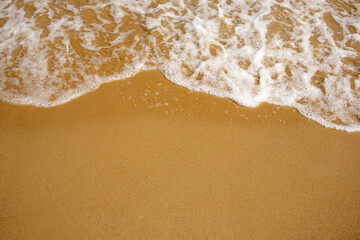 Fototapeta na wymiar Close-up of soft foamy waves on a sandy beach, depicting serene oceanic textures
