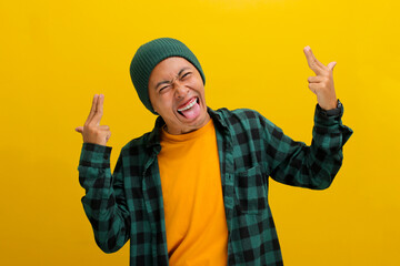 Delighted young Asian man, wearing a beanie hat and casual shirt, playfully makes a finger pistol gesture, winks, and sticks out his tongue, enjoying himself in a lively party atmosphere