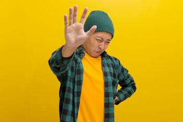 Displeased young Asian man, dressed in a beanie hat and casual shirt, is clearly expressing his...