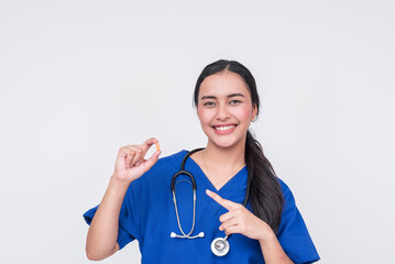 A cheerful young Asian female nurse or caregiver in blue scrubs pointing to a multivitamin...