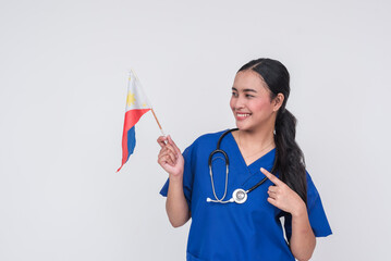 A young Filipino female nurse wearing blue scrubs, pointing to a Philippine flag, her home country.