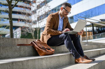 Focused businessman doing online research over wireless computer while sitting on staircase in city
