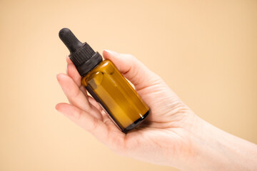 Mockup of a glass bottle with a dropper cap in female hands. Amber colored container with cosmetic...
