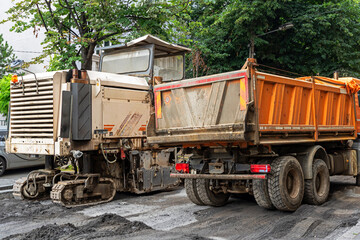 Fototapeta na wymiar Machine for paving work on asphalt next to a tipper truck outside on the street