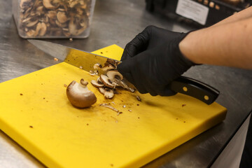 Hand cutting mushroom on top of a chopping board inside the kitchen of a restaurant