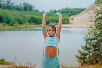 Young girl stretching with a yoga strap outdoors by a river, demonstrating flexibility and exercise