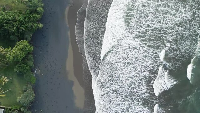 Top view of the black beach on the Indian Ocean. Coast of the island of Bali. Aerial drone footage of ocean waves reaching shore.
