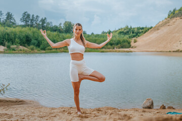 Woman in a Tree Pose (Vrikshasana) by a river, wearing a white yoga outfit, showcasing balance and tranquility
