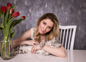 portrait of a pretty girl with a gray cat and red tulips at home.