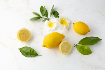 Fresh lemon whole and sliced fruits with citrus leaves on light marble table background.