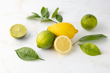 Fresh lemon  and lime whole and sliced fruits with citrus leaves on light marble table background.