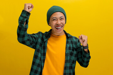 Excited young Asian man, dressed in a beanie hat and casual shirt, is expressing joy and...