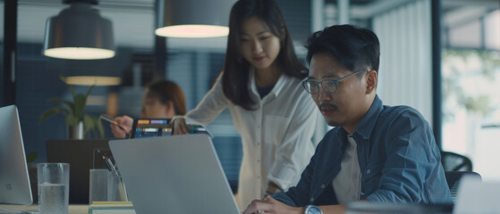 Focused colleagues analyzing data on a laptop in a modern office space.