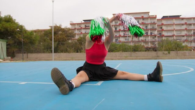 Cheerleader Girl Sitting In Blue Field Shakes Pompoms