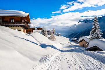 Road in alpine village with traditional wooden houses in winter mountain snow landscape,...