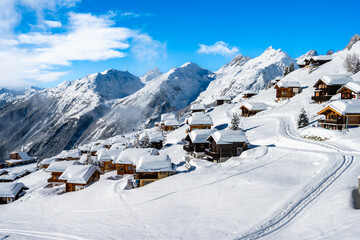 Walking path in winter alpine village with wooden houses and mountains in background, Loetschental...