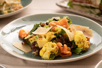 Salad of salted salmon, Parmesan cheese, cauliflower and mixed greens on a plate. Restaurant menu