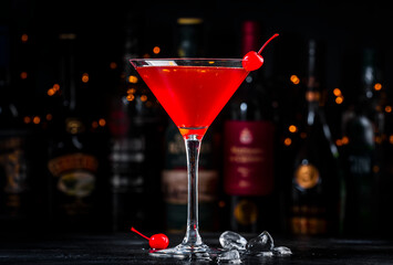 Red alcoholic cocktail drink with cherry on dark background, bar counter with bottles