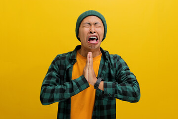 A comical young Asian man, dressed in a beanie hat and casual shirt, is holding his hands in a...