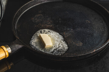A piece of butter is melted in a cast-iron pan. The beginning of cooking.