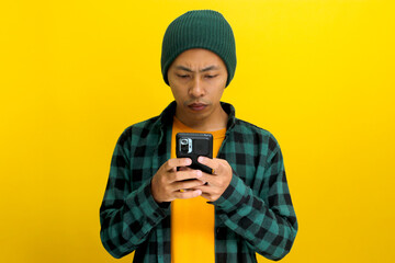 Happy and amazed Asian man, sporting a beanie hat and casual shirt, is using his smartphone for...