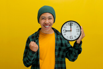 Young Asian man, dressed in a beanie hat and casual shirt, celebrates success with a raised arm in...