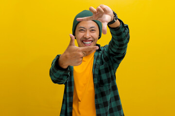 Happy young Asian man, filled with inspiration, is imagining how to capture an interesting shot. He's making a frame gesture with his hands and fingers, as if framing the composition for a photograph
