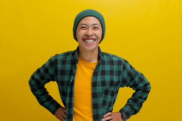 optimistic young Asian man, dressed in a beanie hat and casual shirt, stands confidently with arms...