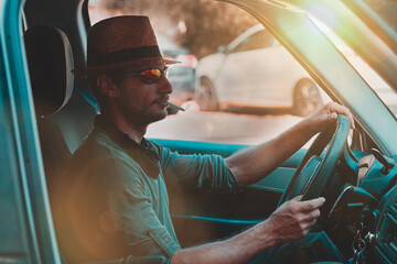 A stylish man sporting a fedora hat and sunglasses is focused on the road while driving. The...