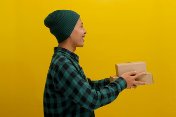 A side view of a young Asian man dressed in a beanie hat and casual clothes, holding a cardboard...