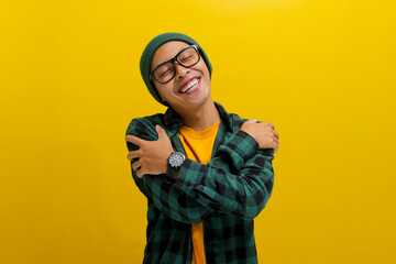 Young Asian man, wearing a beanie hat and casual shirt, hugs himself, symbolizing the concept of...