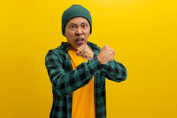 Young Asian man, wearing a beanie hat and casual outfit, is displaying aggression with a defensive...